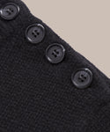 Close-up of the Grace Crewneck, a textured black cashmere sweater featuring four black buttons along the edge, set against a plain beige background—a refined expression of luxury knitwear.