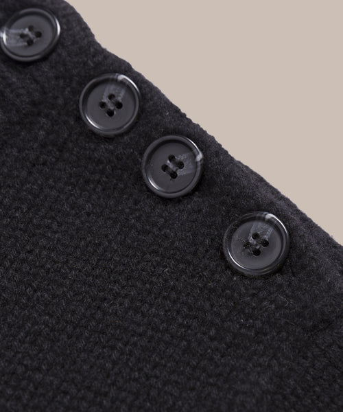 Close-up of the Grace Crewneck, a textured black cashmere sweater featuring four black buttons along the edge, set against a plain beige background—a refined expression of luxury knitwear.
