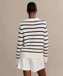 A person with short hair is shown from the back, wearing the Grace Crewneck navy stripe sweater and white shorts, standing against a plain beige background.
