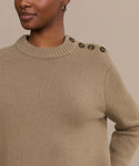 A person wears the Grace Crewneck, a luxurious light brown knit sweater with four dark shoulder buttons, standing against a beige background. Only the upper torso and part of the face are visible in the cropped image.