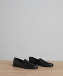 A pair of Griffin Loafer minimalist black shoes made from fine calf leather, displayed side by side on a light wood surface with a plain gray background.