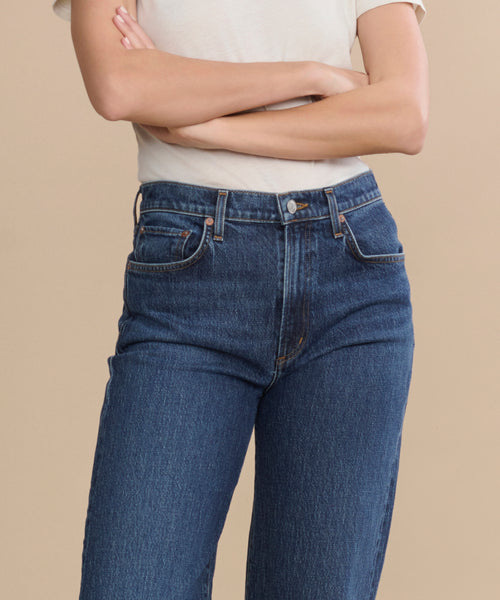 A person in a white short-sleeve shirt and Harper Jean—a relaxed mid-rise, wide-leg style—stands with arms crossed against a plain beige background.