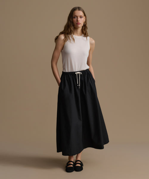 Woman wearing a white sleeveless top and black skirt on a beige background