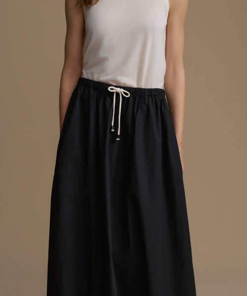 Woman wearing a black skirt with a white top on a brown background