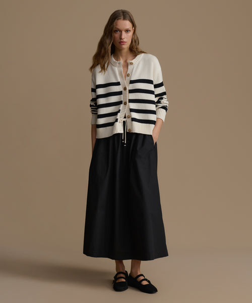 Woman wearing a striped cardigan and black skirt on a beige background