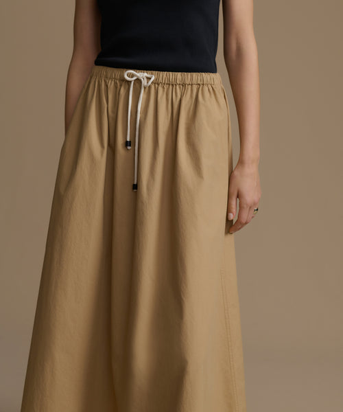 Woman wearing a long beige skirt with a plain background