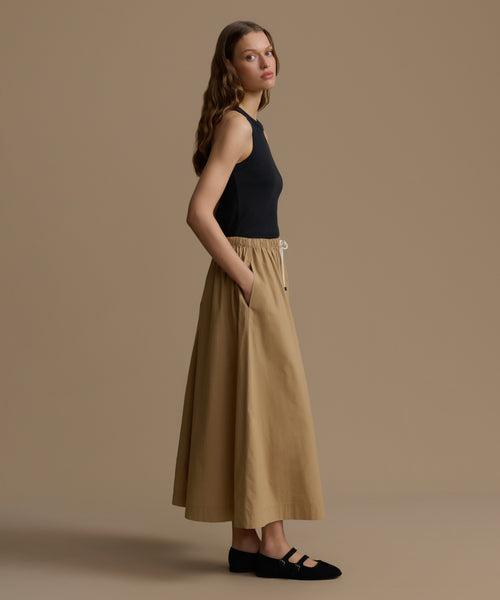 Woman wearing a black top and beige pants against a brown background