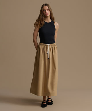 Woman wearing a black top and beige skirt against a brown background