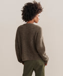A person with curly hair, seen from behind, is wearing the Hayes Crewneck Cardigan and olive green pants, standing against a plain beige background.