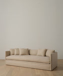 The Dume Sofa, a minimalist beige Hemp piece with five matching cushions and sustainable upholstery, sits on a light wooden floor against a plain off-white wall.