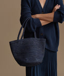 Woman wearing a navy blue cardigan holding a matching navy hollis bag against a beige background
