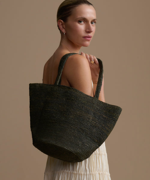 Woman holding an olive woven bag against a beige background
