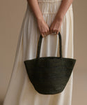 Person holding a olive woven handbag against a beige background