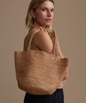 Woman holding a woven brown bag against a beige background