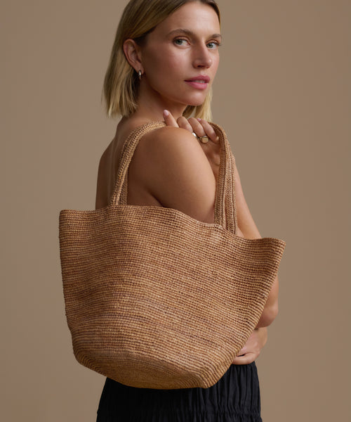 Woman holding a woven brown bag against a beige background