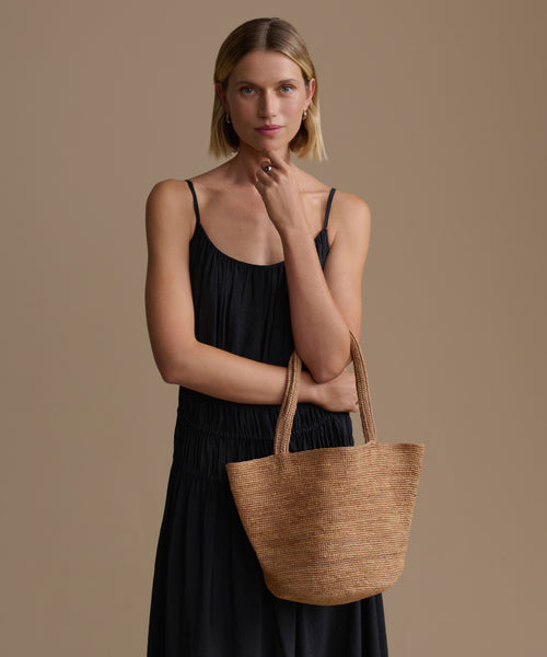 Woman holding a woven handbag against a plain background