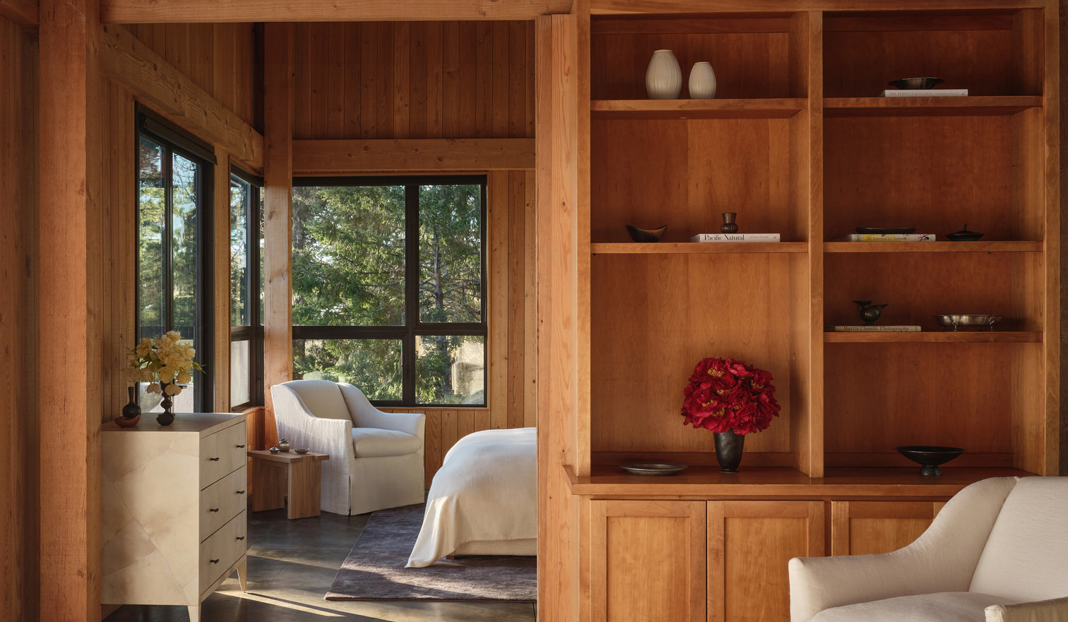 Wooden interior with bookshelf, chairs, and large windows.
