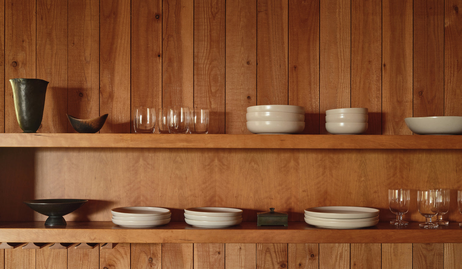Wooden shelves with ceramic bowls and glasses against a wooden wall.