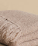 A close-up of the Hudson Throw, a soft, light beige alpaca blanket with fringed edges, folded neatly on a neutral background.