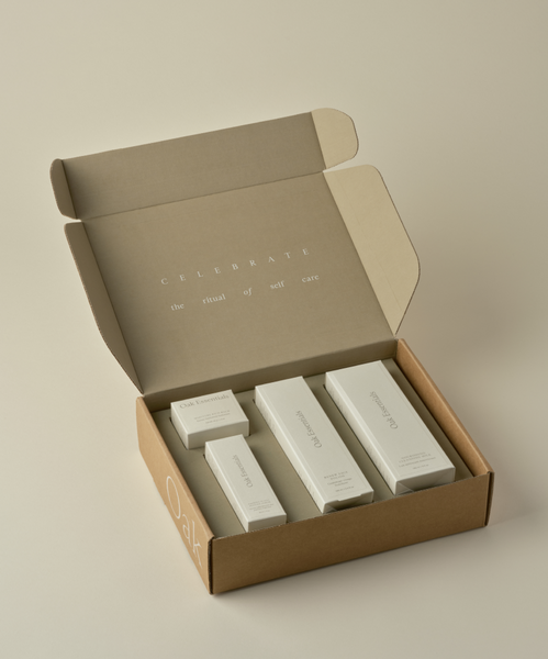 Open brown cardboard box containing neatly arranged The Youthful Skin Routine anti-aging skincare products in white packaging. The inside lid reads, CELEBRATE the ritual of self care.
