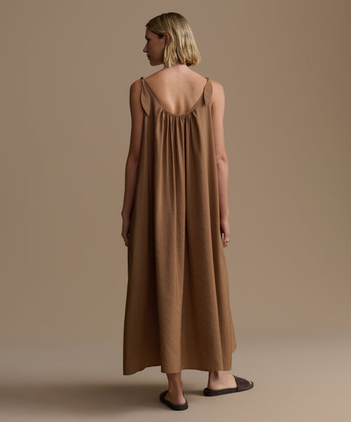 Woman wearing a long brown dress against a beige background