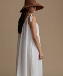 Woman wearing a white dress and brown hat against a beige background