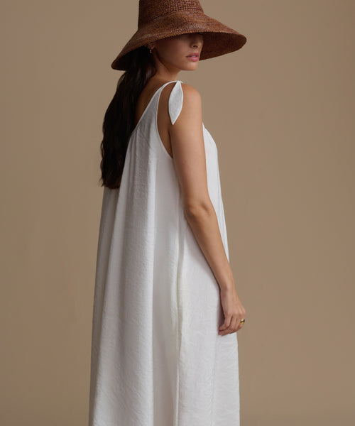 Woman wearing a white dress and brown hat against a beige background