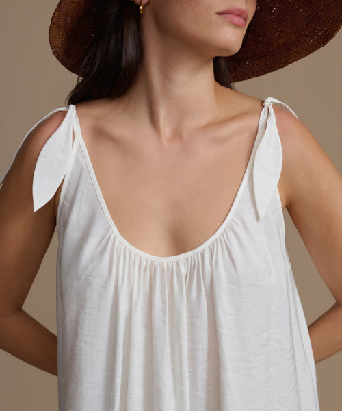 Close-up of a woman wearing a white dress with a brown hat on a neutral background
