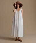 Woman wearing a white dress and brown hat against a beige background