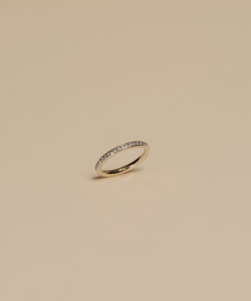 The Iris Eternity Band is a slim 14k solid gold ring featuring small, evenly spaced conflict-free diamonds around the band, shown against a simple beige background.