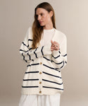 A woman with long brown hair models the Chloe Cardigan in Ivory Navy Stripe over a white top and pants, standing against a neutral background with a relaxed expression.