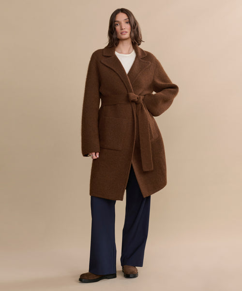 A person stands against a plain beige background, wearing the Jessica Sweater Coat over a white top and navy wide-leg pants.