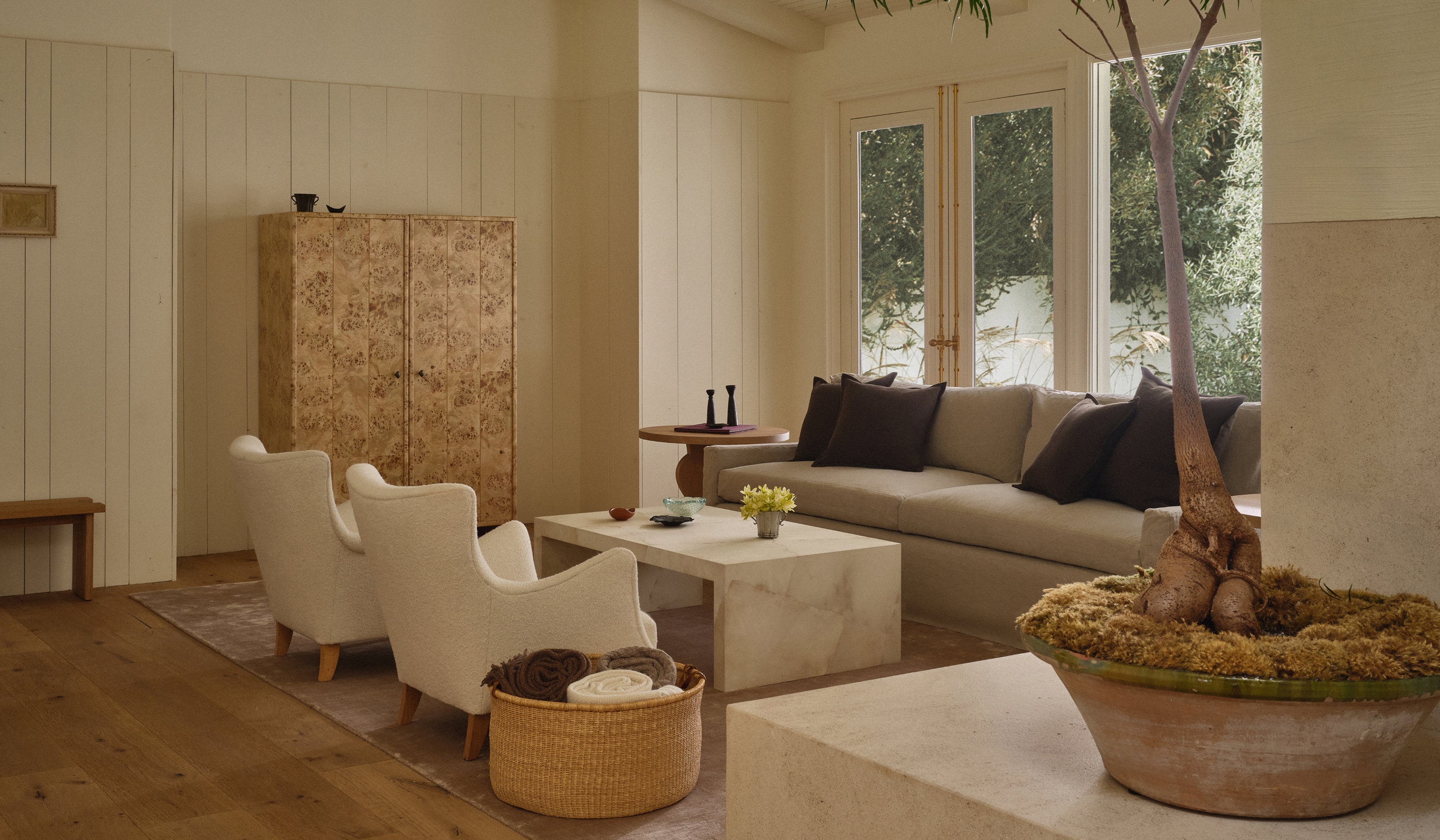Modern living room with beige sofa, white chairs, and a decorative plant.
