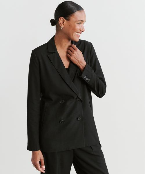 A woman with dark hair in a low bun smiles while wearing the Jones Blazer and matching pants, showcasing a modern power suit against a plain light background.