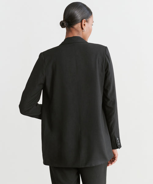 A woman with her hair in a low bun faces away from the camera, wearing the Jones Blazer and matching pants against a plain, light-colored background.