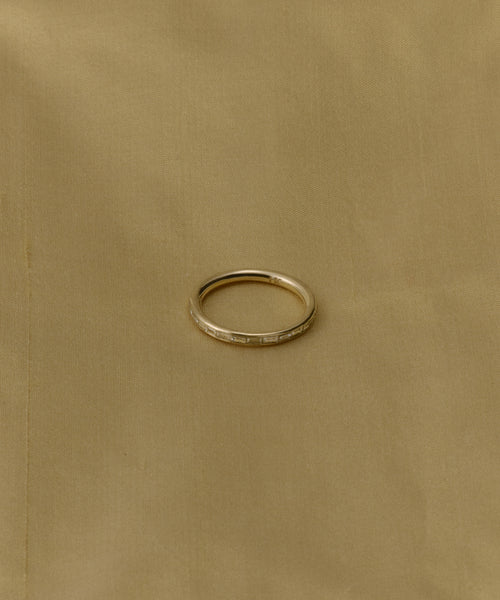 The June Baguette Band from Jenni Kayne Jewelry, a simple diamond yellow gold ring, is centered on a plain beige fabric background.