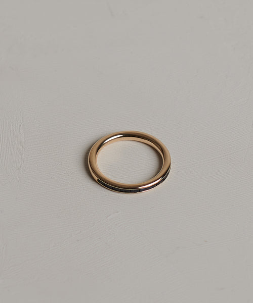 The June Baguette Band, a sleek 14k gold ring, rests on a light gray textured surface.