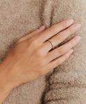 A hand wearing the June Baguette Band in 14k gold rests on soft beige fabric, with neatly trimmed natural nails, highlighting the understated elegance of Jenni Kayne jewelry.
