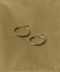The June Baguette Hoops, a pair of simple silver earrings inspired by classic Jenni Kayne designs, are displayed on a light brown fabric background.