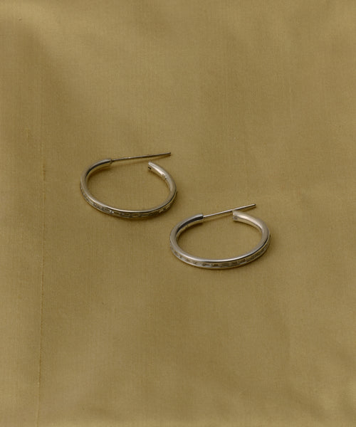 The June Baguette Hoops, a pair of simple silver earrings inspired by classic Jenni Kayne designs, are displayed on a light brown fabric background.