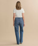A person with shoulder-length hair faces away, wearing a white short-sleeve tee and the Kelly Jean high-rise straight jeans, crafted from sustainable denim, set against a plain beige background.