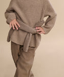 A child wears the Kids' Cashmere Fisherman sweater in undyed stone, styled oversized with rolled-up sleeves and matching wide-leg pants, standing hands on hips against a plain beige background.