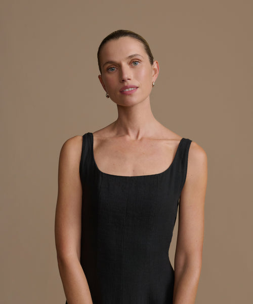 Woman wearing a black sleeveless dress against a beige background