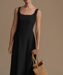 Woman wearing a black dress holding a brown bag against a brown background
