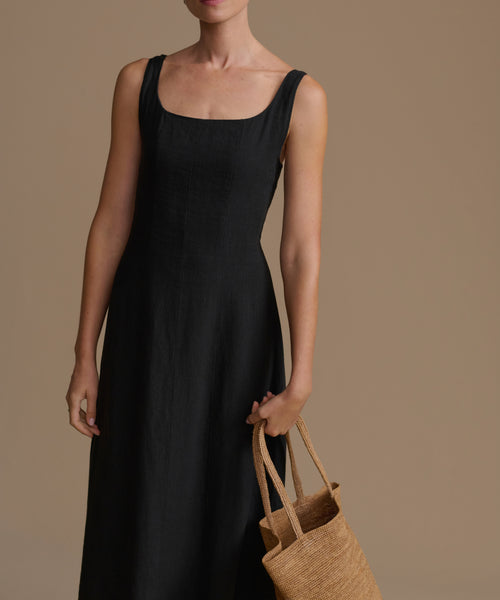 Woman wearing a black dress holding a brown bag against a brown background