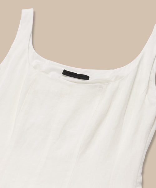A close-up of the Kinney Dress, a sleeveless white linen summer dress with a scoop neckline and black label inside the collar, shown on a beige background.