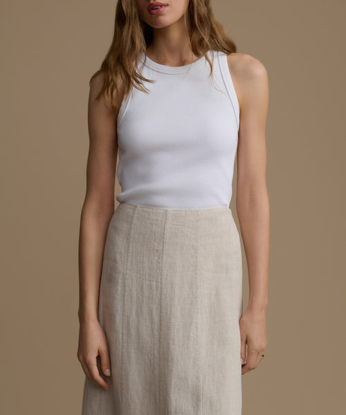 Woman wearing a white tank top and beige skirt against a brown background