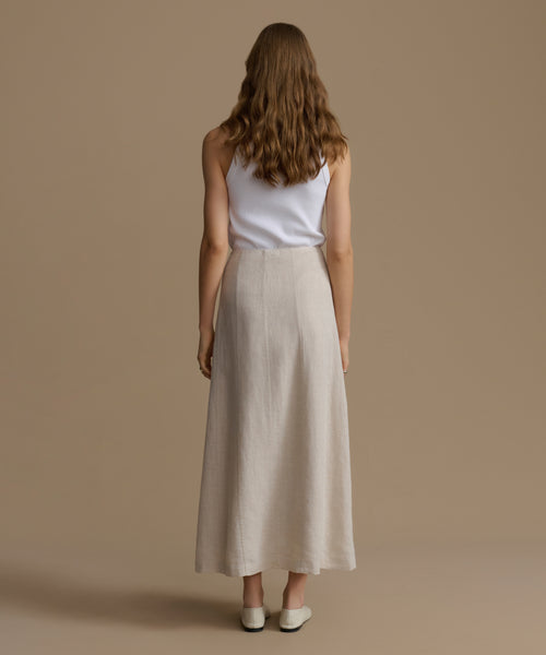 Woman wearing a white top and beige skirt against a brown background