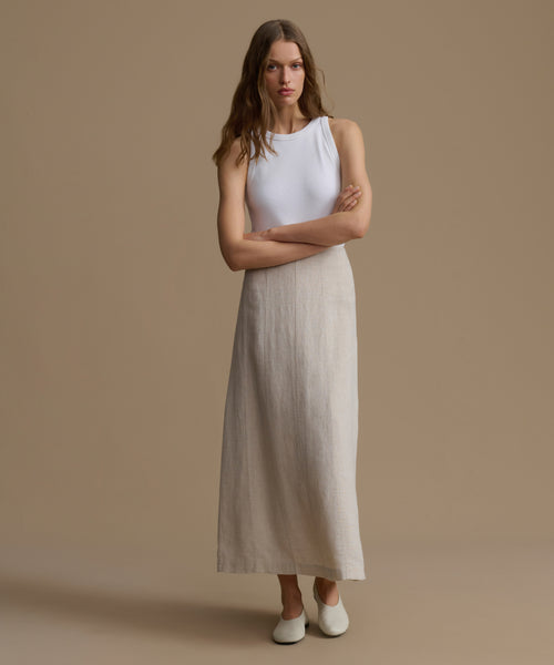 Woman wearing a sleeveless white top and beige skirt against a brown background