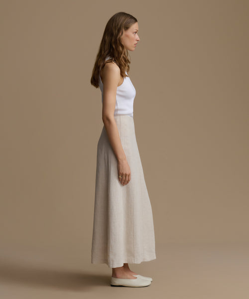 Woman wearing a white sleeveless top and beige skirt against a beige background